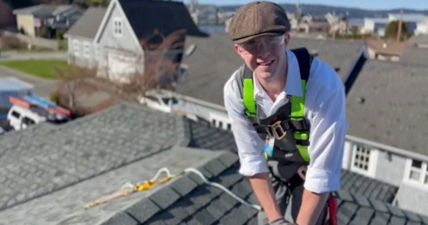 Person on a roof wearing safety gear with houses in the background