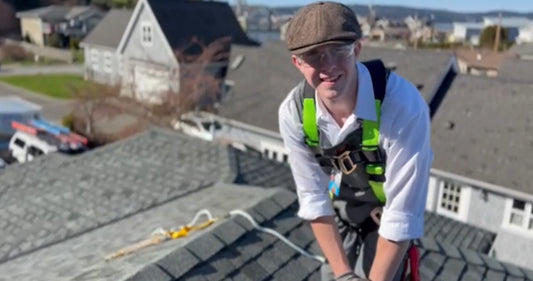 Person on a roof wearing safety gear with houses in the background